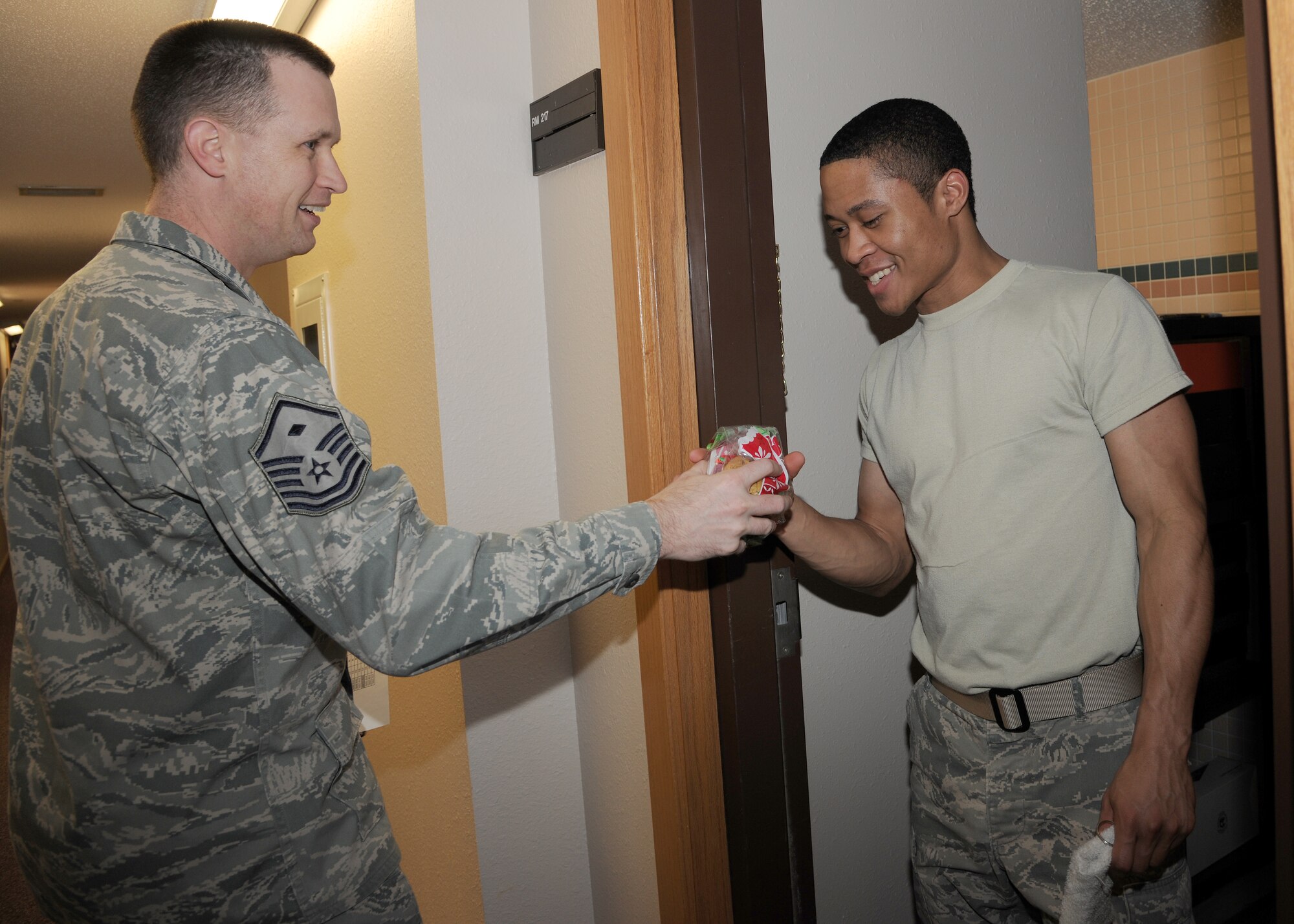 Master Sgt. Patrick Michael, 319th Operations Support Squadron first sergeant, delivers cookies to Senior Airman Obed Salazar, 319th OSS, on Dec. 5 at Grand Forks Air Force Base, N.D.  Every year military spouses and the wing first sergeants surprise the Airmen who live in the dorms with a taste of the upcoming holiday to boost their morale.   (US Air Force photo by Airman 1st Class Ashley N. Taylor)