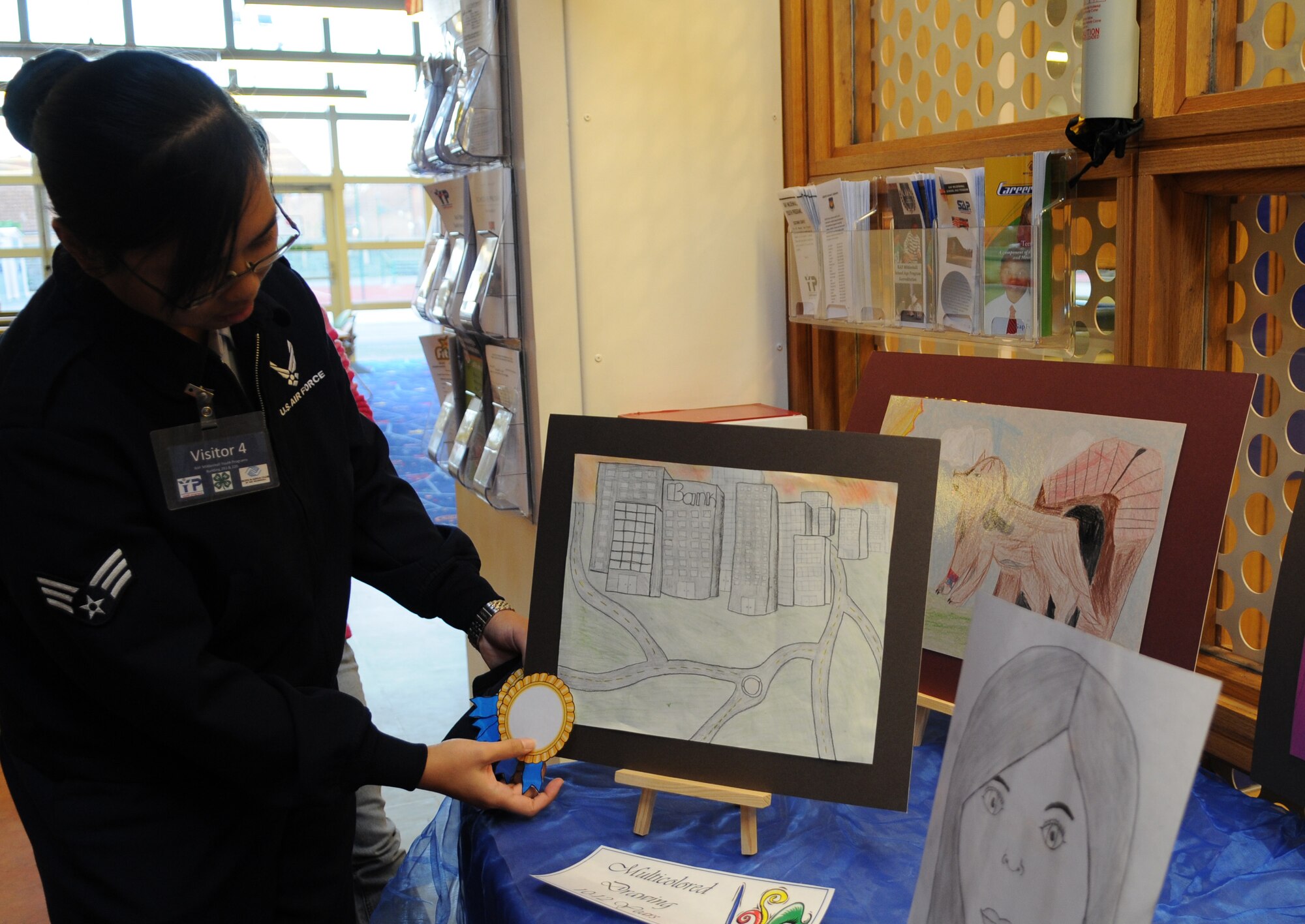 RAF MILDENHALL, England – Senior Airman Jerilyn Quintanilla, 100th Air Refueling Wing Public Affairs, awards a ribbon to the multicolored drawing 10 to 12-year-old category during judging of the Boys & Girls Club of America 2012 National Fine Arts Exhibit at the youth center here, Dec. 5, 2011. Categories included monochromatic drawing, pastel, watercolor, oil or acrylic, print making, mixed media, collage, sculpture, and a group project. The program was open to youth ages 6 to 18, and the winner from each category will have their artwork displayed at the Bob Hope Community Center Dec. 12 through 16. (U.S. Air Force photo/Senior Airman Rachel Waller)