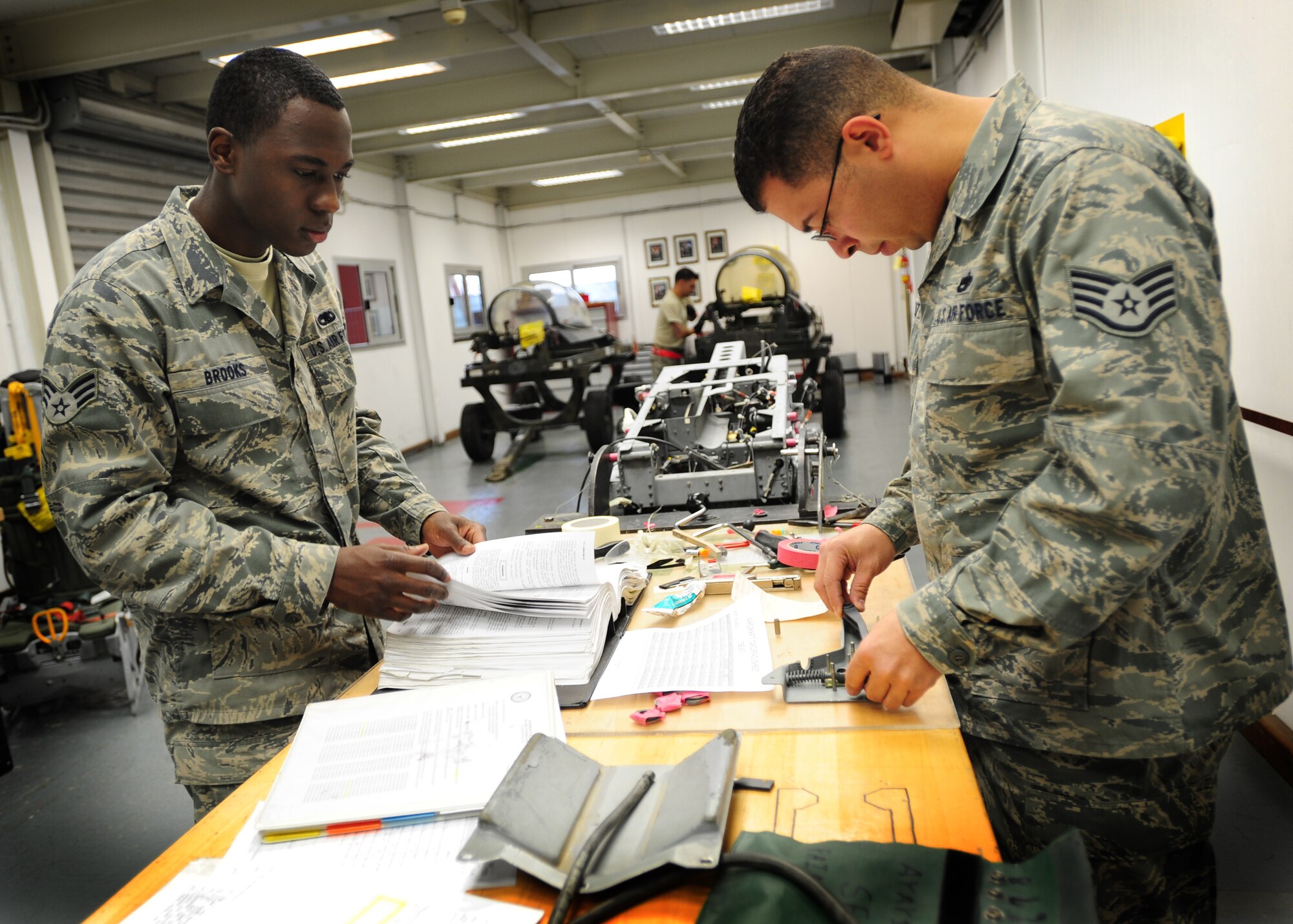 (From Left) Senior Airman Corey Brooks, aircrew egress systems journeyman, and Staff Sgt. Edwin Cruz, aircrew egress systems technician 31st Maintenance Squadron, prepare to inspect an ejection seat Dec. 5 at Aviano Air Base, Italy.  Aircrew egress systems technicians maintain aircraft egress systems including ejection seats, canopies, hatches, modules, subsystems, and related support equipment.  (Staff Sgt. Evelyn Chavez)