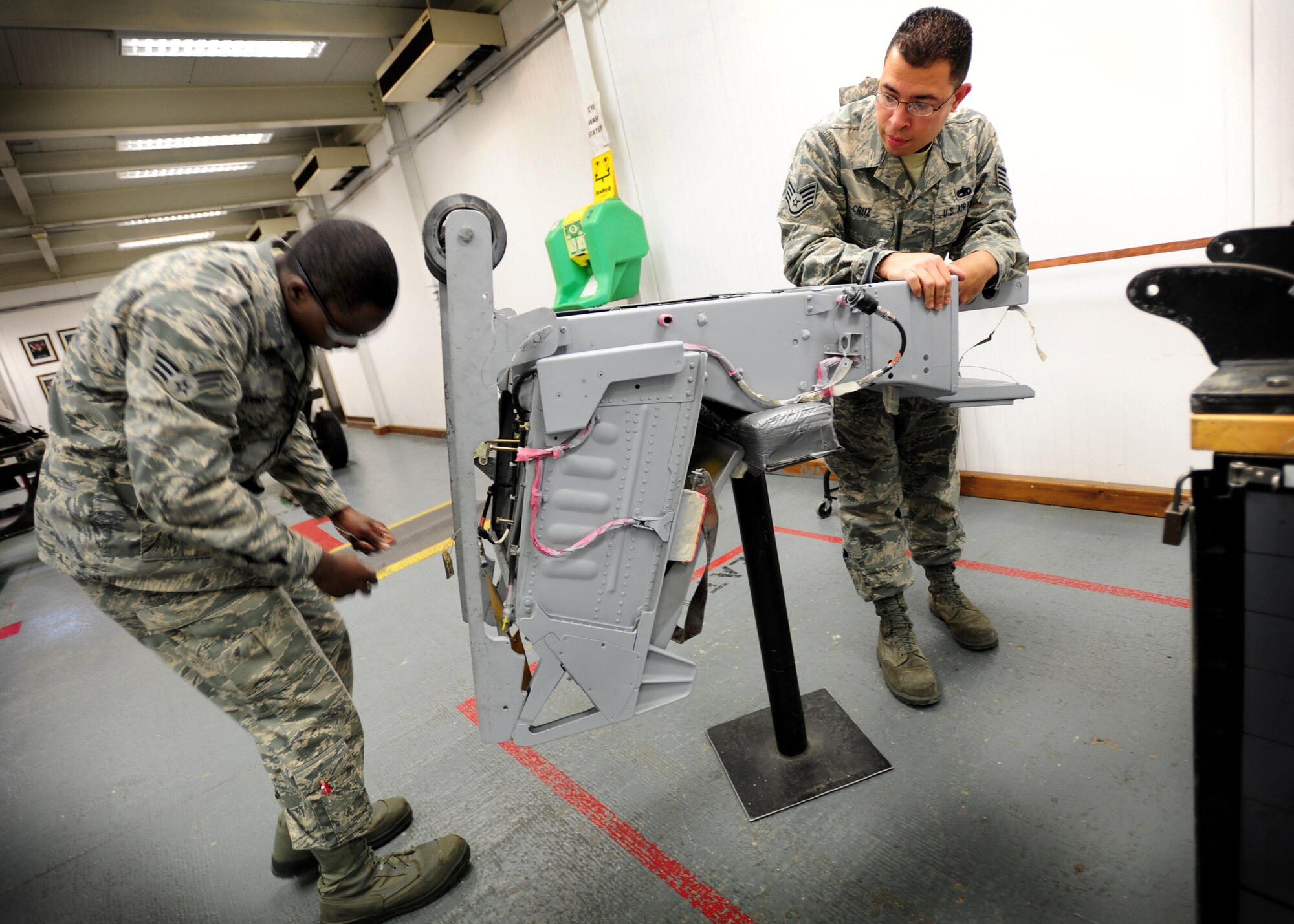 (From Left) Senior Airman Corey Brooks, aircrew egress systems journeyman, and Staff Sgt. Edwin Cruz, aircrew egress systems technician 31st Maintenance Squadron, repair an ejection seat Dec. 5 at Aviano Air Base, Italy.  Aircrew egress systems technicians maintain aircraft egress systems including ejection seats, canopies, hatches, modules, subsystems, and related support equipment.  (Staff Sgt. Evelyn Chavez)