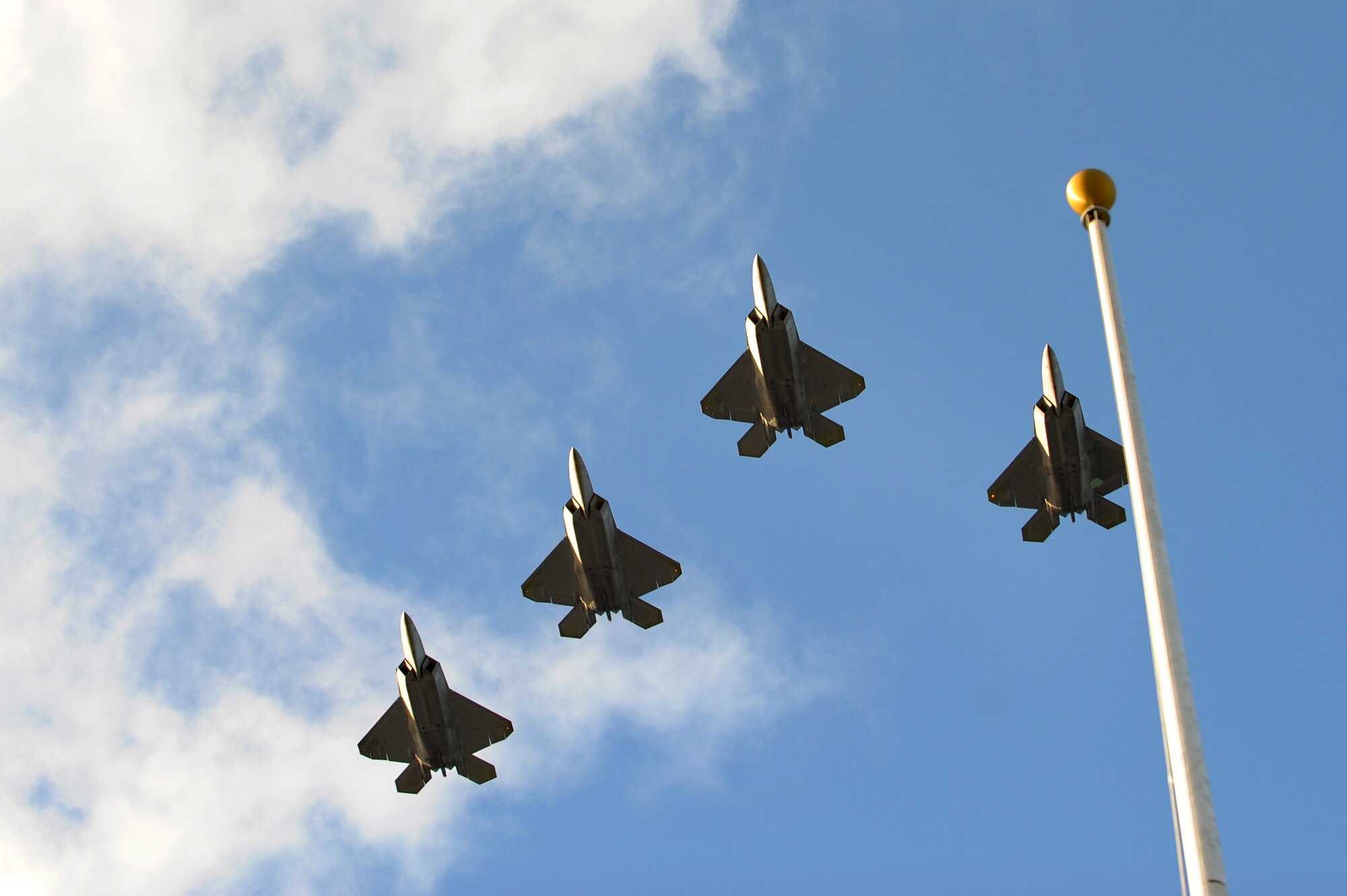 Four F-22 Raptors, assigned to the 19th and 199th Fighter Squadrons, Joint Base Pearl Harbor-Hickam, Hawaii, fly a missing-man formation over the Atterbury Circle flag pole during the 70th Anniversary Remembrance Ceremony, commemorating the attacks on Hickam Field Dec. 7, 1941. The fighter squadrons are a joint partnership between the active duty and Hawaii Air National Guard. (U.S. Air Force photo/Staff Sgt. Mike Meares)