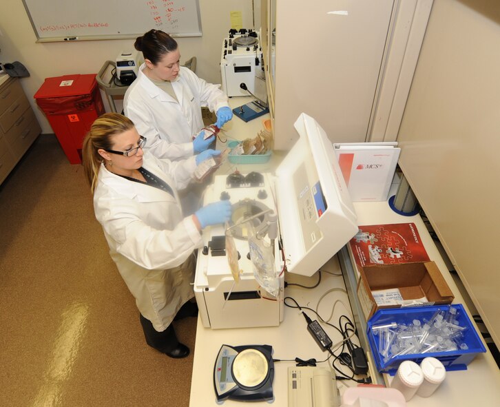 Sarah Torres and Master Sgt. Rosemary Roe,  process porcine whole blood units to be separated and glycerolized for frozen storage of red blood cell components at David Grant USAF Medical Center, Dec. 6. The porcine blood components are used to enable the best trauma care training possible for residents and technicians. (U.S. Air Force photo/ Staff Sgt. Liliana Moreno)