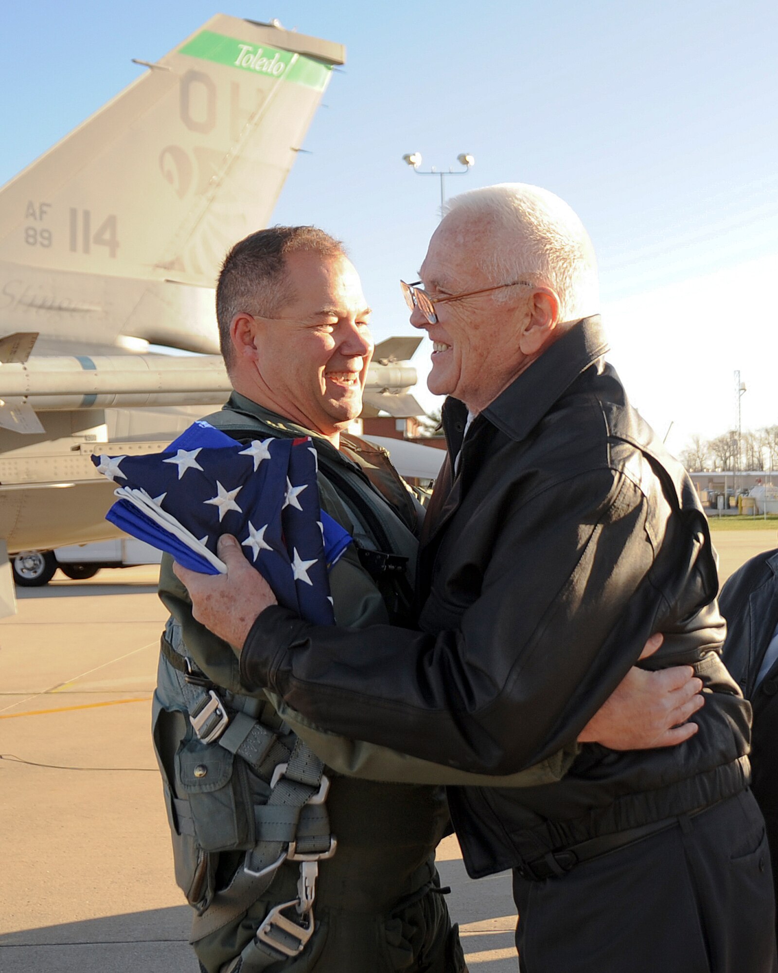 Lt. Col. Tim Moses, 180th FW Operations Support Squadron Commander, receives a hug from Walter Young after Moses presented Mr. Young with an Air Force flag in honor of Young's son, Lt. Mike Young. Moses carried with him an American flag and a United States Air Force flag and flew up the coast of Lake Huron and over the crash site, where a memorial in Lt. Young’s name now stands. 180th Fighter Wing members, along with family and friends of pilot, Lt. Mike Young gathered for a small memorial honoring the pilot, 20 years after Young died when his A-7 Corsair crashed during a routine training mission. The group gathered at the 180th Fighter Wing, Ohio Air National Guard Base, Swanton, OH, Nov. 30.