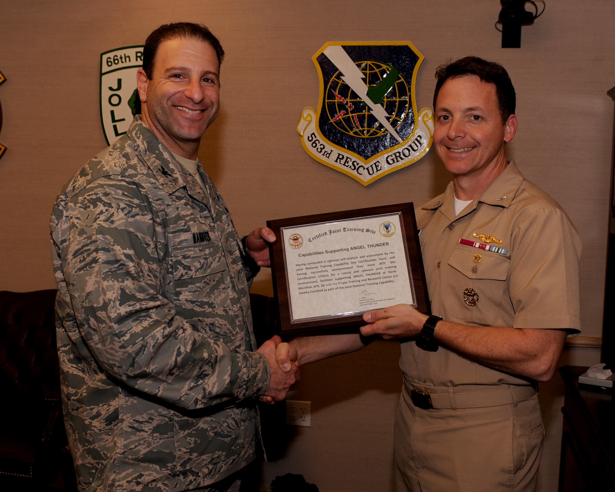 U.S. Air Force Col. Jason Hanover, 563rd Rescue Group commander, accepts a plaque from U.S. Navy Capt. Chris Harkins, JNTC division chief of the operations and plans division, at Davis-Monthan Air Force Base, Ariz., Nov. 30, 2011. The plaque is a certification and accreditation towards the Angel Thunder exercise held every year at D-M. (U.S. Air Force photo by Airman 1st Class Christine Griffiths/Released)