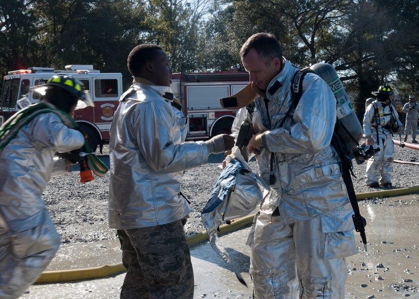 A member of the 23rd Civil Engineer Squadron fire department assists U.S. Air Force Col. Billy Thompson, 23rd Wing commander, with putting on his personal protective equipment during a live-fire training session at Moody Air Force Base, Ga., Dec. 5, 2011. Chief Master Sgt. Frank Batten, 23rd Wing command chief was also in the training. Other 23rd CES Airmen guided Thompson and Batten through the training to deter flames and exit safely. (U.S. Air Force photo by Senior Airman Eileen Meier.Released)