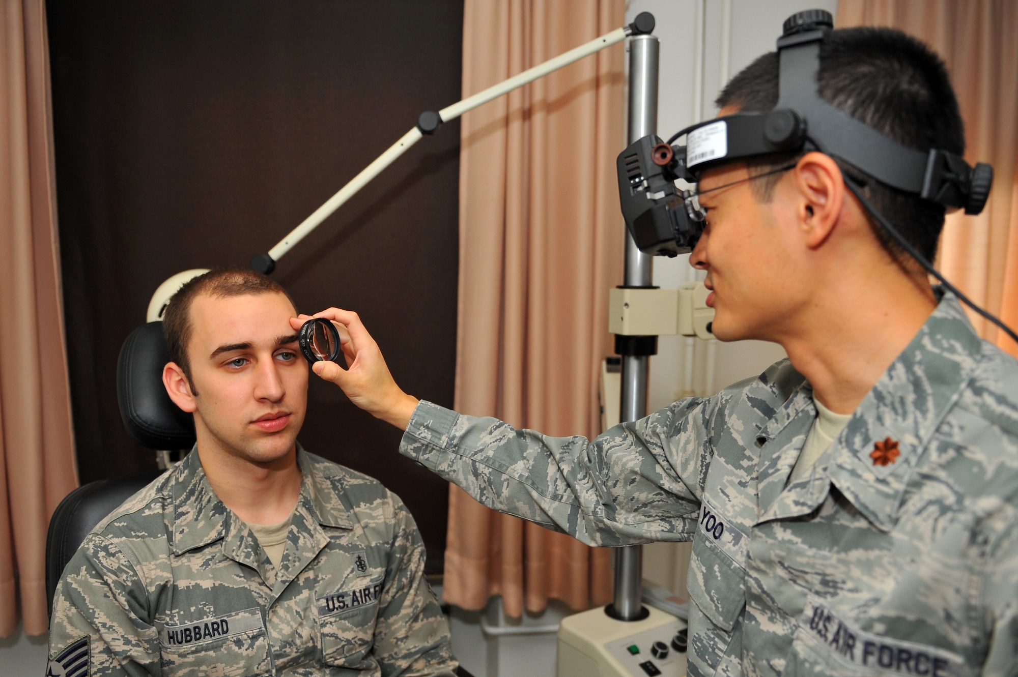 SPANGDAHLEM AIR BASE, Germany – Maj. (Dr.) Richard Yoo, right, 52nd Aerospace Medicine Squadron optometrist, uses a binocular indirect ophthalmoscope to view the ocular interior of Staff Sgt. Nicholas Hubbard, 52nd AMDS ophthalmic technician, during a follow-up eye exam at the optometry clinic here Dec. 6. The AMDS provides vision correction as well as diagnosing, treating and managing ocular diseases to keep Airmen fit to fight and their family members healthy. (U.S. Air Force photo/Airman 1st Class Dillon Davis)