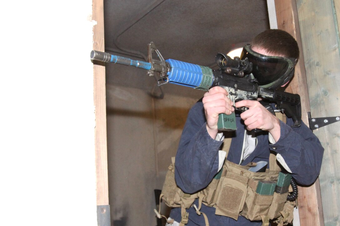 Dressed as an insurgent, Cpl. Doug Brown, an operator at the Infantry Immersion Trainer with Training Support Division, aims down a hallway in an effort to suppress fire. Dressed as an insurgent, Cpl. Doug Brown, an operator at the Infantry Immersion Trainer with Training Support Division, crouches behind a low wall and takes aim.