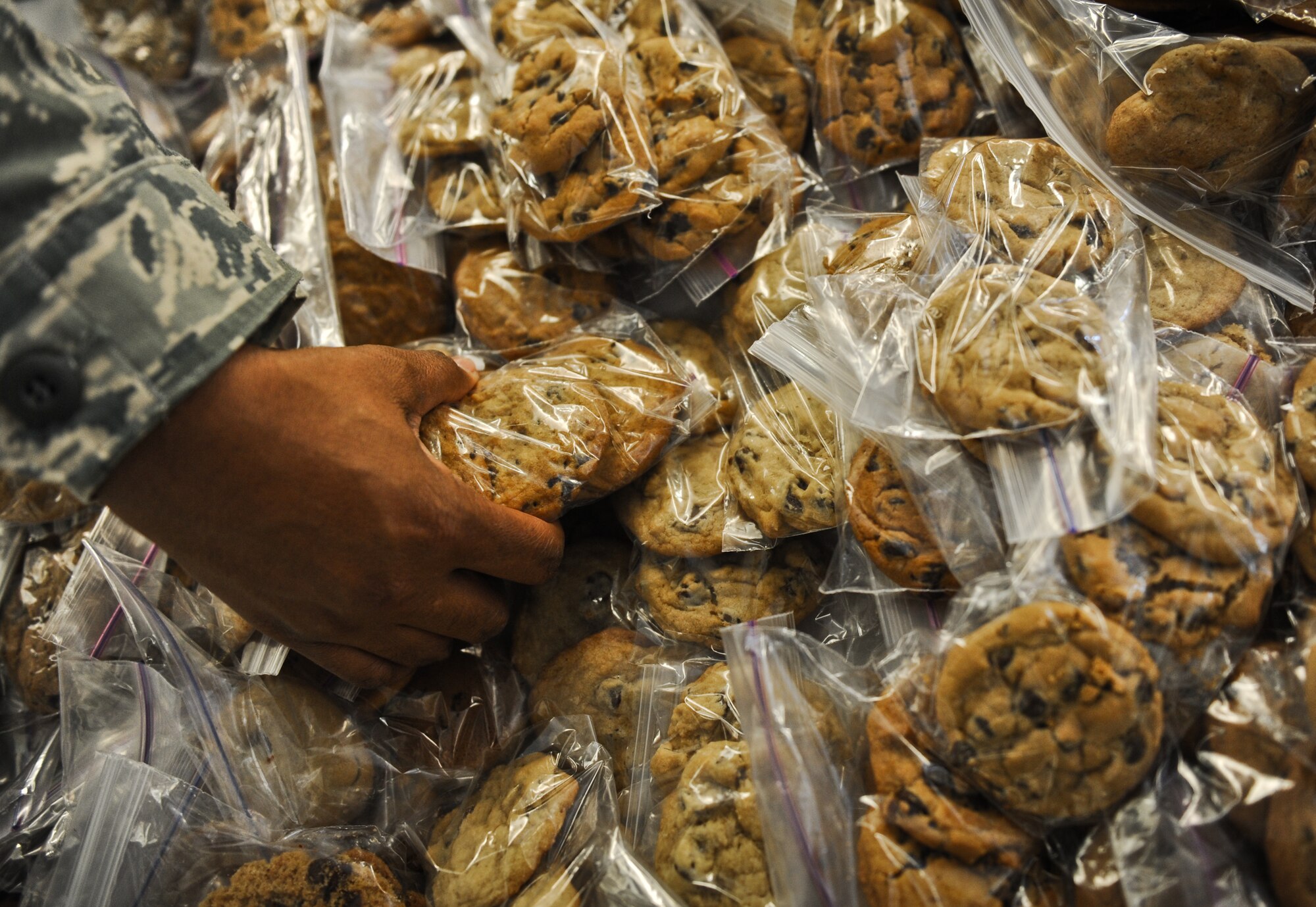 A volunteer for the Annual Cookie Caper event, grabs a bag of cookies to put in a colorfully decorated bag for single Airmen in the dorms on Joint Base Pearl Harbor-Hickam, Hawaii, Dec. 8. The extra cookies left over from the event will be given to the 24 hour agencies on base, such as Security Forces and the gate guards. (U.S. Air Force photo/Senior Airman Lauren Main)