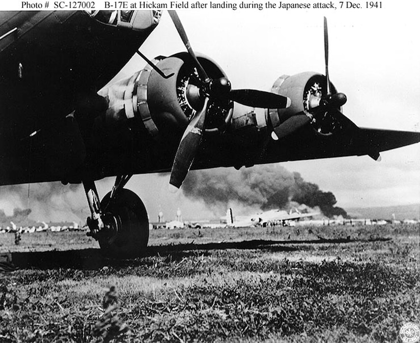 A U.S. Army B-17E at Hickam Air Field, after landing safely during the Japanese air raid. In the background is a B-17C (or B-17D). Smoke from burning ships at Pearl Harbor is visible in the distance. (Courtesy Photo/Air Force Accessions)