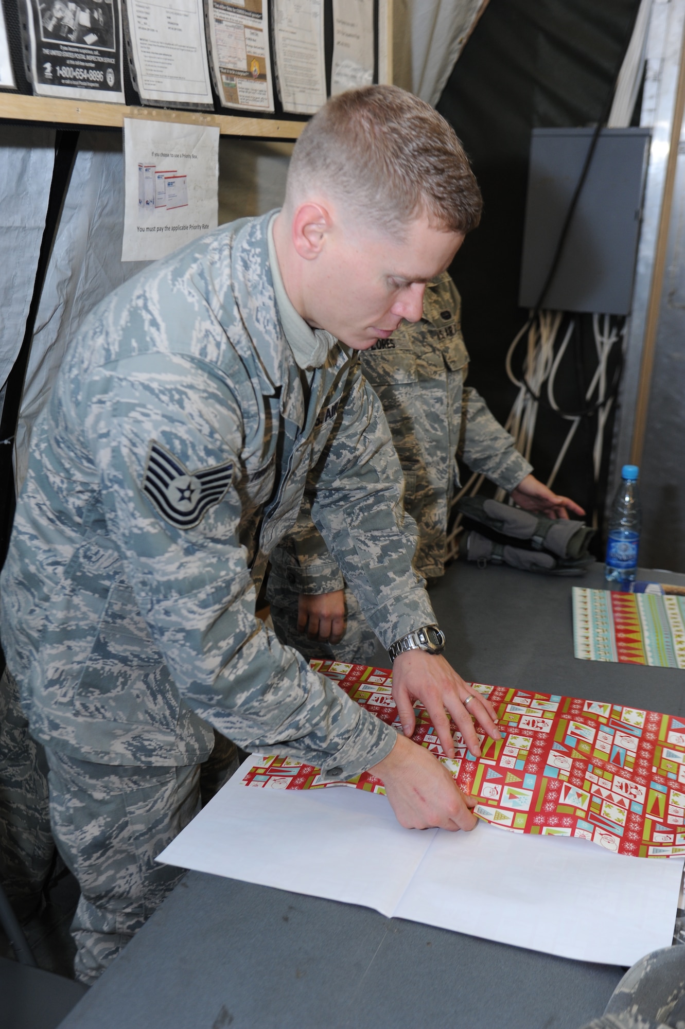 Tech. Sgt. Aaron Tibbits, 376th Expeditionary Communications Squadron communication security, wraps gifts for people mailing Christmas gifts home in the post office at the Transit Center at Manas, Kyrgyzstan, Dec. 7, 2011.  The Transit Center Top 3 organization raised money by accepting donations to wrap gifts before mailing. Tibbits is deployed from the 1st Communication Maintenance Squadron, Kapaun Air Station, Germany. (U.S. Air Force Photo/Tech. Sgt. Hank Hoegen)