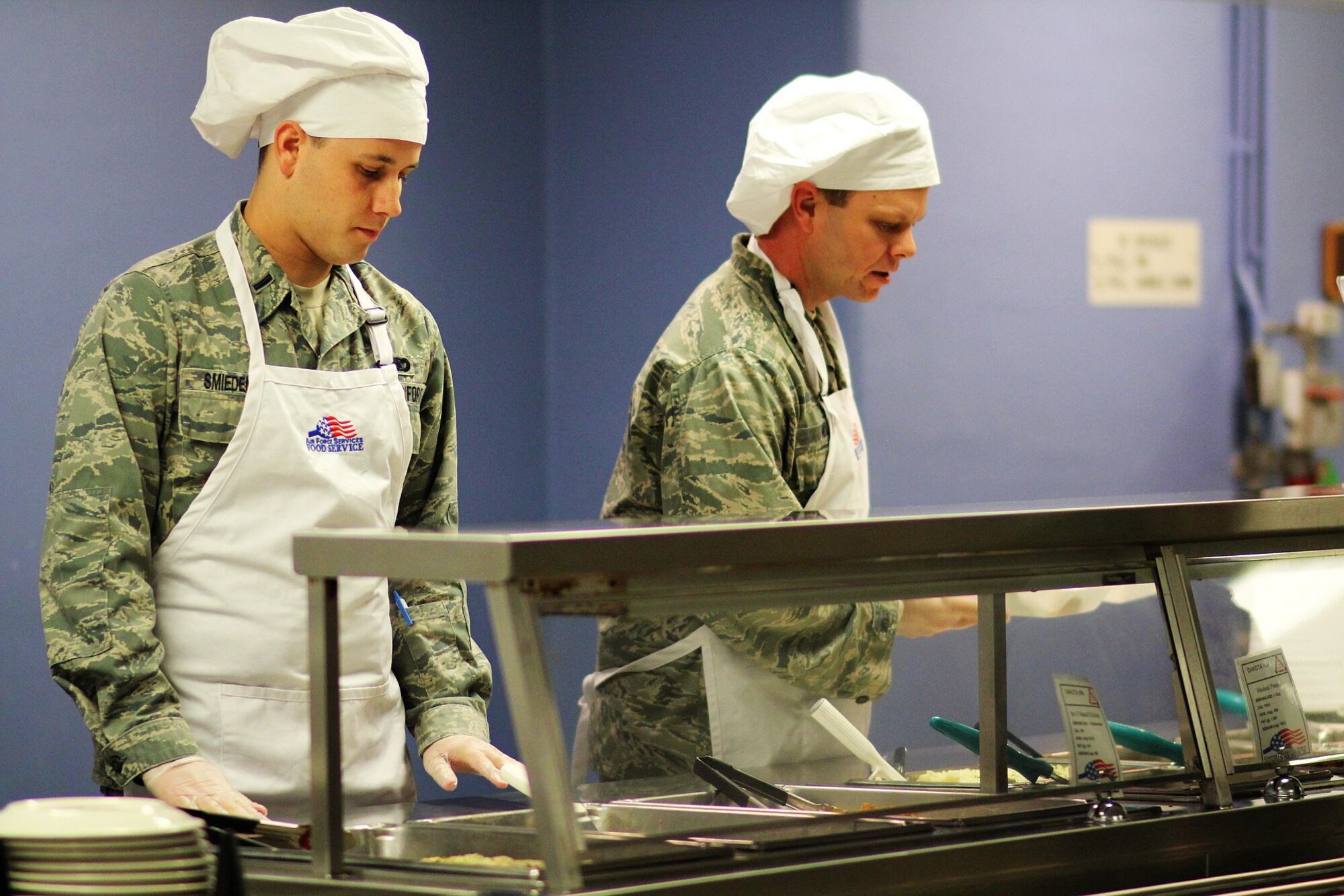 MINOT AIR FORCE BASE, N.D. -- 1st Lts. Ross Smiedendorf, 5th Security Forces Squadron, and Jeremy Miller, 5th Force Support Squadron, volunteer their time at the Dining Facility here to serve young enlisted Airmen meals. The officers provide this monthly community service as part of the Minot AFB Company Grade Officers’ Council outreach. (U.S. Air Force photo/Capt. Jon Arceta)