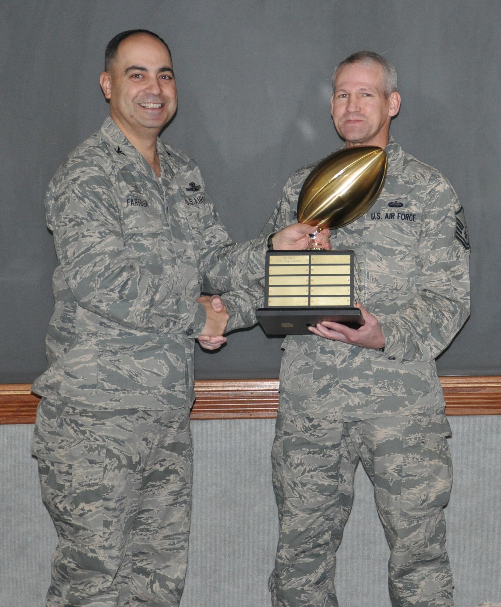 Col. George Farfour, 90th Missile Wing vice commander, presents Master Sgt. Shelton Humphries, 90th Maintenance Group NCO-in-charge of knowledge operations, the Commander’s Cup during a wing stand-up meeting held in the wing conference room Nov. 30. Humphries accepted the trophy on behalf of the 90th MXG, who went undefeated again in flag football. (U.S. Air Force photo by Senior Airman Mike Tryon)