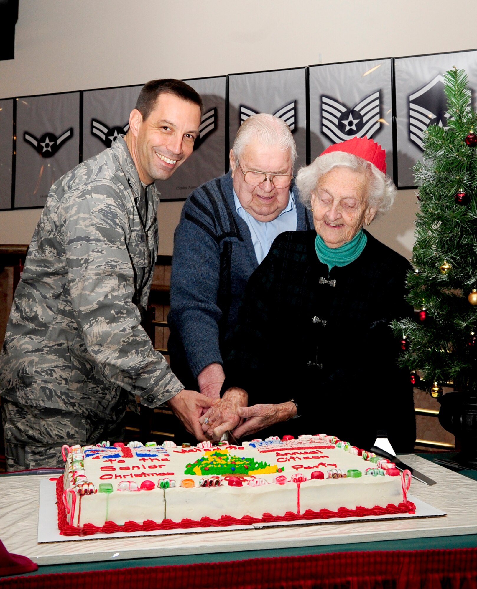 RAF MILDENHALL, England – Col. Christoper Kulas, 100th Air Refueling Wing commander, assisted by Jim Clements and Caroline Francks, cuts the cake during the 30th Annual Senior Citizen Christmas Lunch here Dec. 7, 2011. Local British residents Clements, 92, and Francks, 90, were the most senior of the guests attending the Christmas lunch that gave Team Mildenhall members the opportunity to get to know the local community.  (U.S. Air Force photo/Senior Airman Ethan Morgan)