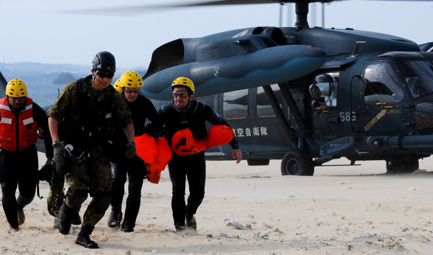A pararescueman from the Japan Air Self Defense Force leads a group of water casualties from a JASDF UH-60J Rescue Wings helicopter during Cope Angel 12 in Okinawa, Japan, Dec. 5, 2011. The 33rd and 31st Rescue Squadrons paired up with partners from the Japan Air Self Defense Force during Cope Angel to train on water and land rescue and triage tactics. (U.S. Air Force photo by Airman 1st Class Maeson L. Elleman/Released)