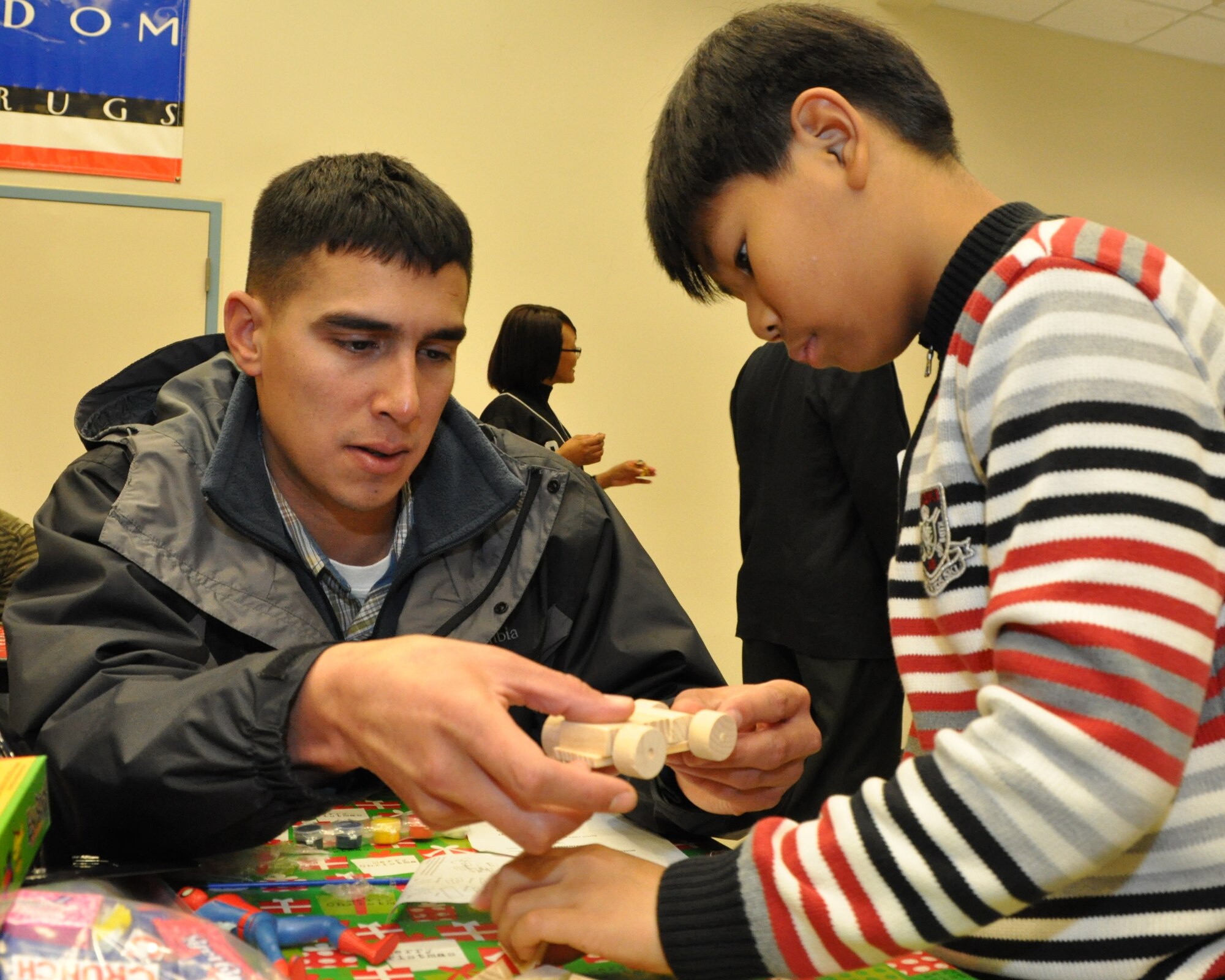 Staff Sgt. Rey Solis, 51st Logistics Readiness Squadron, assists his Korean buddy with piecing together a wooden race car at the Pearl S. Buck Foundation Christmas party Dec. 10, 2011, in the Osan middle school.  Crafts included decorating Christmas tree ornaments, building wooden models, decorating miniature trees, and coloring pictures.  (U.S. Air Force photo/Senior Master Sgt. Stuart Camp)