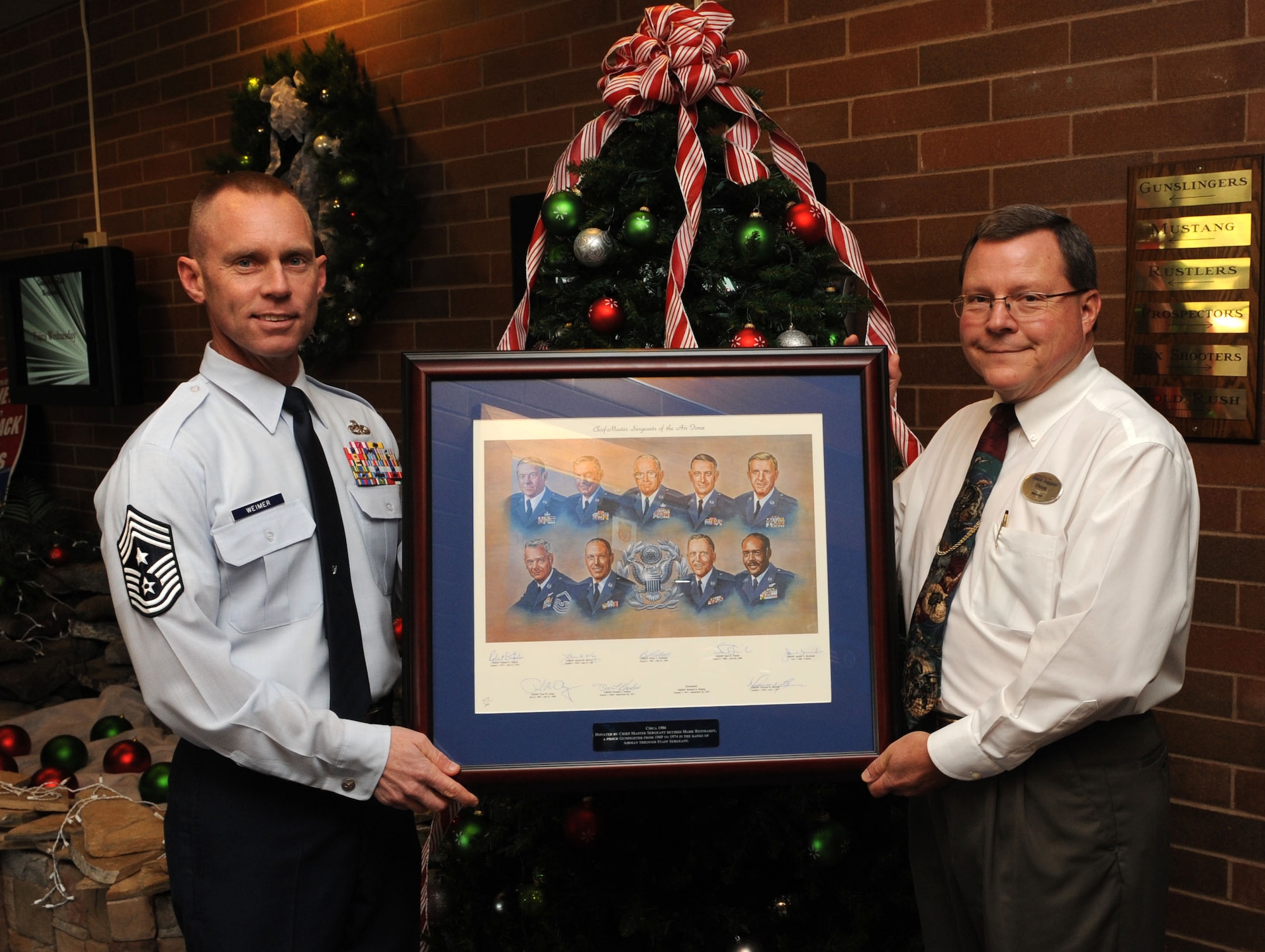 Chief Master Sgt. John Weimer, 366th Fighter Wing command chief, presents a lithograph to the Doug Rhodes, Gunfighter Club manager, at Mountain Home Air Force Base, Idaho, Dec. 12, 2011. The lithographs were donated by retired Chief Master Sgt. Mark Reinhardt – one will be on display at the Airman Leadership School and the other at the Gunfighter Club. (U.S. Air Force photo by Senior Airman Debbie Lockhart)