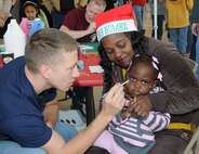 JaMyra Palmer, held by guardian Alberta White, gets decorated. Children on base were served up a special breakfast Dec. 3 at the Honor Guard hangar. Santa Claus was available to hear children's gift requests and the children worked on Christmas crafts. (Air Force photo/Wendy Simonds)
