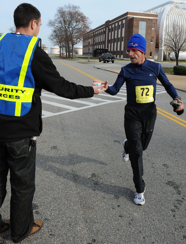 U.S. Air Force Senior Airman Jonathan McClenny, Air Combat Command A3 weapons system administrator, hands water to retired Master Sgt. Kevin Barry at the 7-mile marker during the “Race ‘Round the Base” at Langley Air Force Base, Va., Dec. 10, 2011. Volunteers set up water stations to keep runners hydrated and motivate participants. (U.S. Air Force photo by Airman 1st Class Teresa Cleveland/Released) 