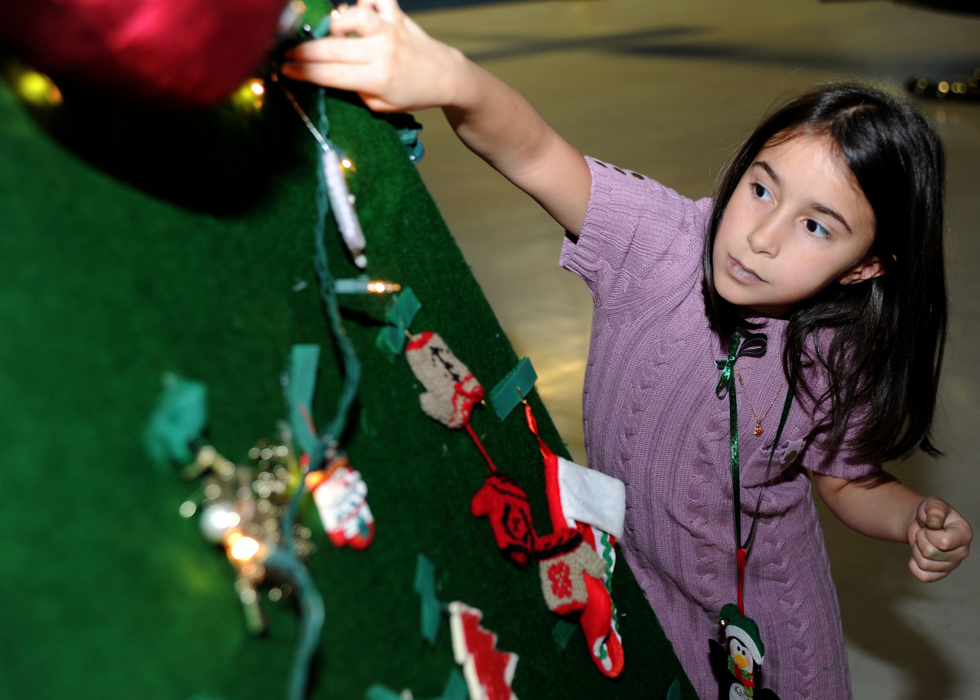 Kialani, 8, daughter of Karl Briales from Lorton, Va., places an ornament on a Christmas tree during the Parents and Children Fighting Cancer holiday event in Hangar 3 on Dec. 3. This is the third year the family has attended the holiday event. (U.S. Air Force photo/Senior Airman Bahja J. Jones) 