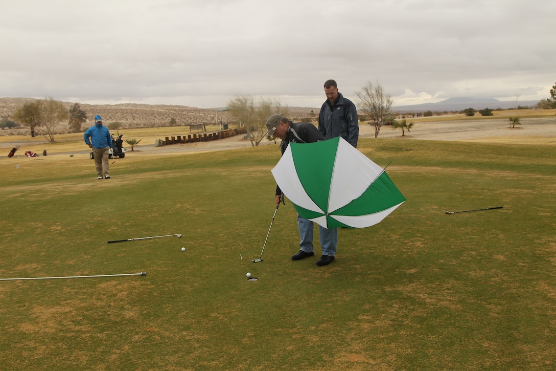 Ron Genet shows off his skill by successfully putting the ball with an umbrella in his other hand green during the Commanding General’s Holiday Four-Person Golf Tournament at the Desert Winds Golf Course Dec. 13, 2011.