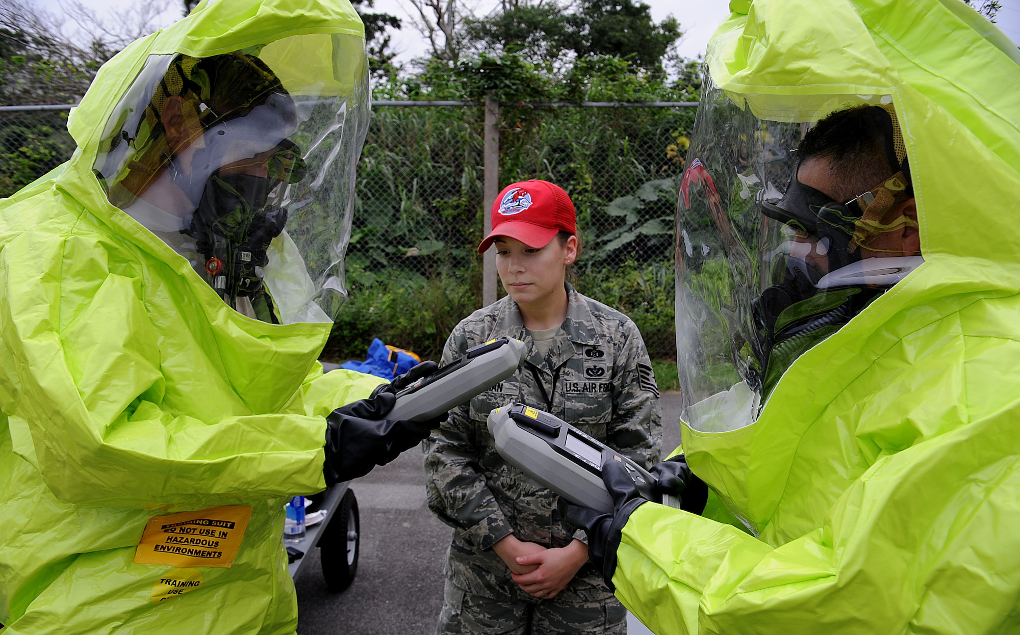 U.S. Air Force Tech. Sgt. Sophia Inman, Detachment 1, 554th RED HORSE Squadron NCO-in-charge of emergency management, instructs U.S. Air Force Capt. Paul Gregory, 18th Wing Command Post deputy chief, and U.S. Air Force Chief Master Sgt. William Plaza, 18th Force Support Squadron superintendant, on procedures for using the Ahura 1st Defender electronic system while in their Level A protection gear, Dec. 13, 2011, at Kadena Air Base, Japan. Capt. Gregory and Chief Plaza were two of many Kadena Airmen that toured RED HORSE Squadron facilities to learn about the unit's unique mission. (U.S. Air Force photo by Staff Sgt. Christopher Hummel/Released)