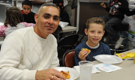Chief Master Sgt. Jose LugoSantiago and his son, Adrian, eat pizza at the Youth Holiday Party at Joint Base Charleston  -Air Base Dec. 10. The Youth Center put together a Holiday Party for kids of all ages and had fun stations including: "VanDoren" the Magician, a bounce house, dart throwing, mini-golf, face painting, free food and a surprise appearance from Santa Claus. LugoSantiago is the 628th Air Base Wing command chief. (U.S. Air Force photo/Airmen 1st Class Ashlee Galloway)