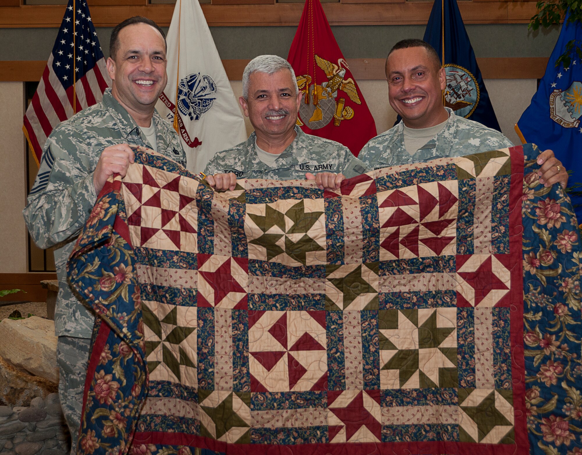 Chief Master Sgt. David Fish, Air Force Mortuary Affairs Operations chief enlisted manager (left), and Sgt. 1st Class Luis Valle (right), present a Quilt of Valor to Sgt. 1st Class Jimmy Toro  Dec. 9, 2011, at the Charles C. Carson Center for Mortuary Affairs, Dover Air Force Base, Del., Volunteers from around the world make quilts for veterans and service members touched by war. (U.S. Air Force photo/Staff Sgt. Agustin Salazar)