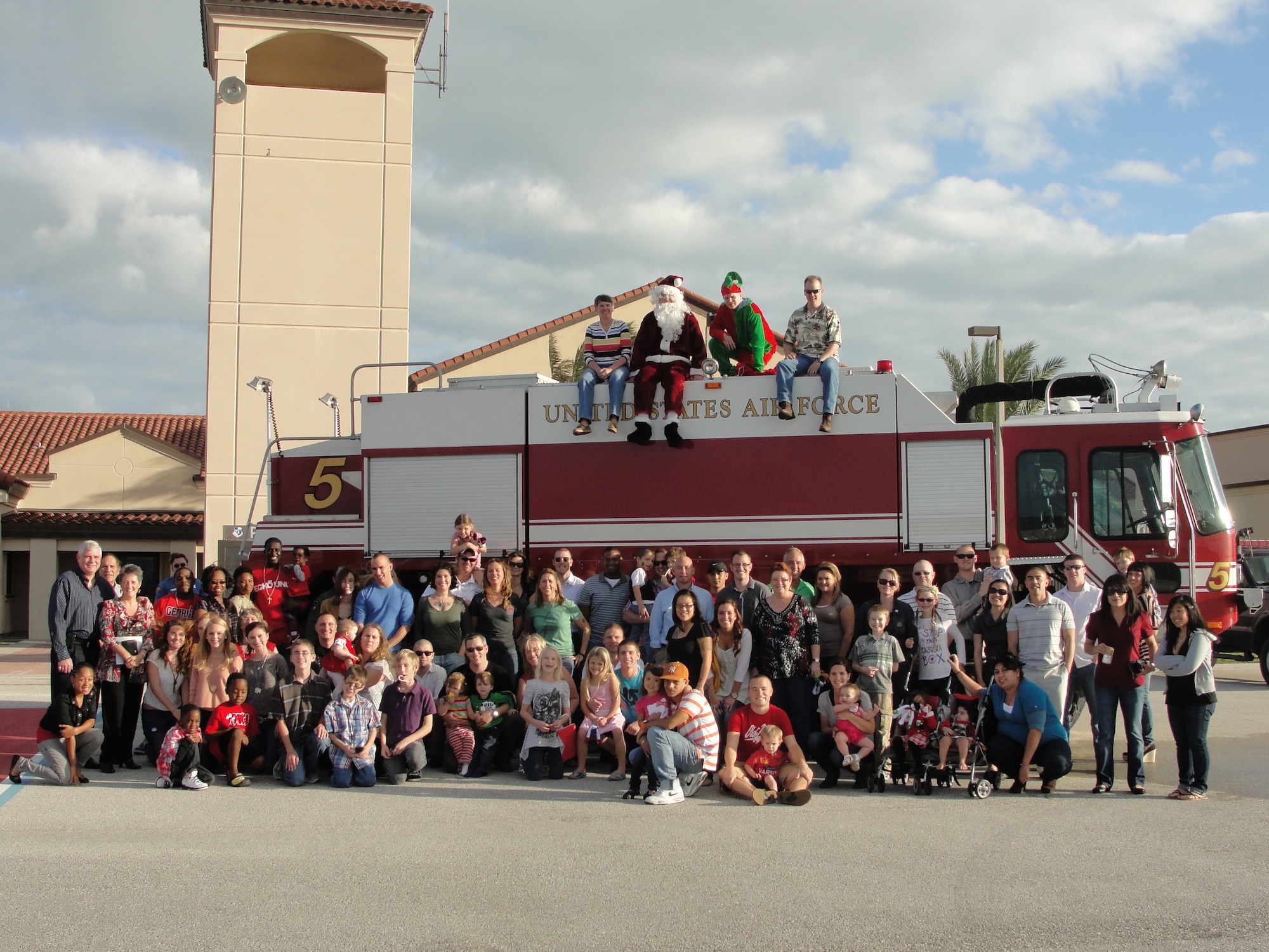 Members and families of the 45th Operations Support Squadron pose for a group photograph outside Patrick Base Operations with (left to right atop fire truck) 45th Operations Group Commander Col. Denette Sleeth, Santa, Santa’s Helper and 45 OSS Commander Lt. Col. Patrick Youngson during the squadron’s annual Holiday Party. “We had a great turnout and the kids had a ball, especially with the arrival of the
base fire truck,” said Colonel Youngson. (Air Force photo/Senior Airman Jacklyn Arango-Morales)