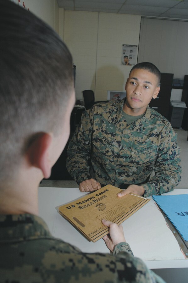 Lance Cpl. Cameron Perry, administrative specialist with Marine Corps Logistics Base Albany, receives a service record book from a Marine at the counter inside Military Personnel Center, recently.