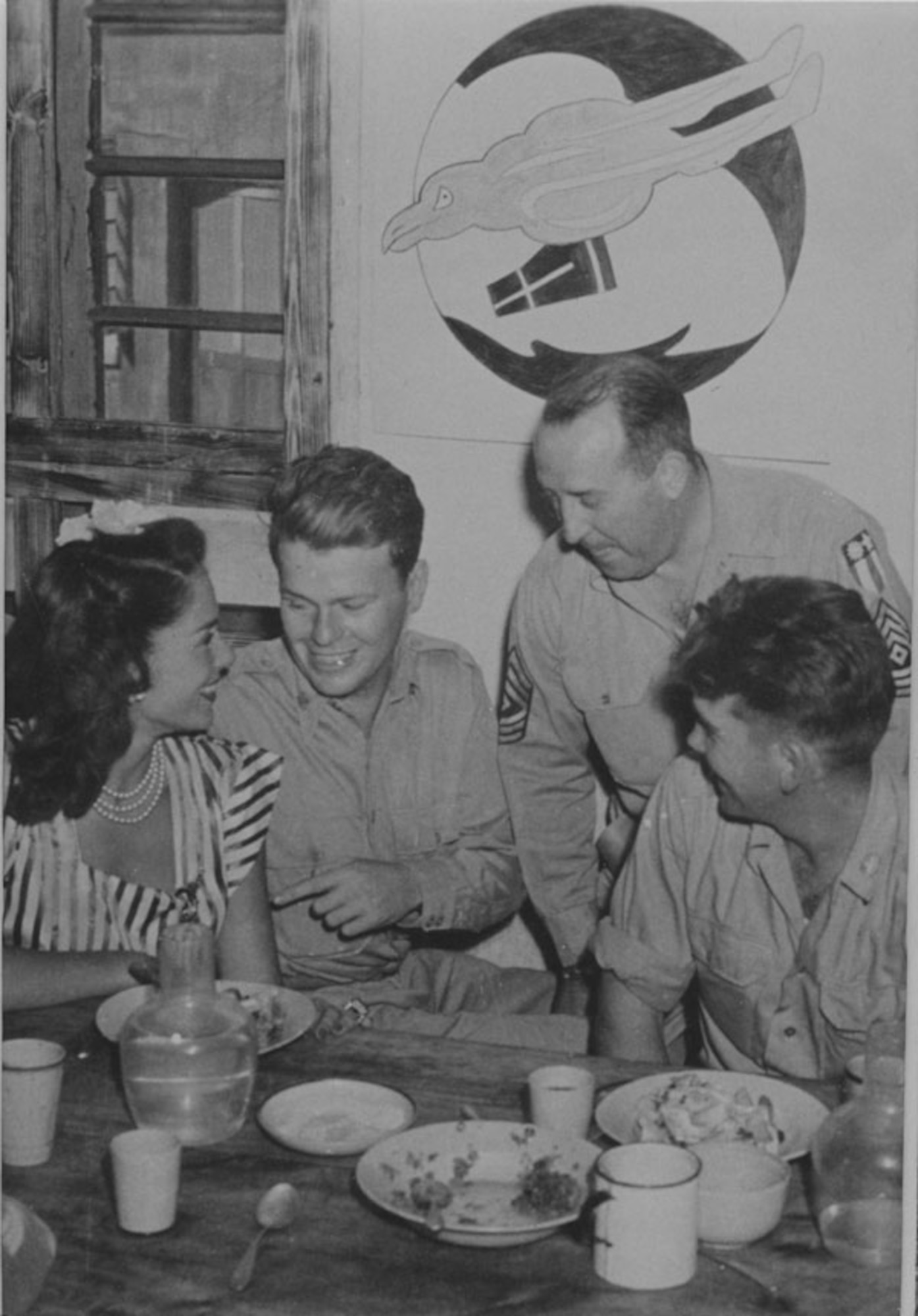 Members of the 35th PRS entertain Jinx Falkenburg.  From left to right are Jinx, Lt. Morris, First Sergeant Flavin and Sgt Shaylor.  First Sergeant John Flavin and Sgt Jack Shaylor were original members of the Oregon National Guard’s 123rd Observation Squadron.  Note the early Redhawk emblem of the squadron on the wall behind, with twin tails evocative of the twin-boomed F-5 recon aircraft the squadron flew in the CBI.  The Redhawk is still used by the ORANG’s 123rd Fighter Squadron today.