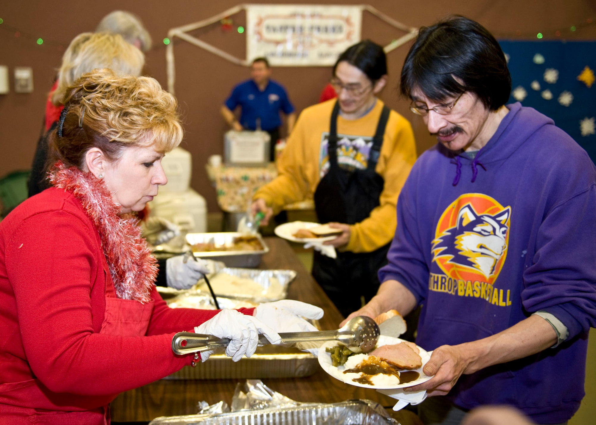 Jeanne Fox, a volunteer for the Bering Strait Native Corporation, serves green beans to Clyde Ongtowasruk of Wales, Dec. 9. Fox along with another three dozen volunteers from Anchorage was in Wales for an Operation Santa Claus mission.   (National Guard photo/MSgt. Shannon Oleson)
