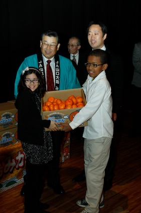 Matthew C. Perry Elementary School student counsel members display Mikan fruit with Motoi Yoshimura, Yamaguchi Oshima Agricultural Cooperative Association president and Yoshihiko Fukudo, Iwakuni City mayor during the 2nd annual Mikan Exchange at the Sakura Theater here Dec. 15. A Mikan is a small fruit simialr to a tangerine.