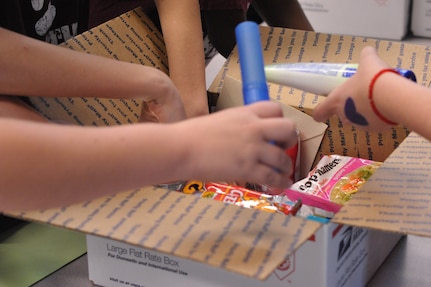 Sixth-graders from Schlater Intermediate School put snack and toiletries in a postal box during Operation Shoebox Dec. 9. Operation Shoebox shipped "shoeboxes" to 35 deployed members. (U.S. Air Force photo by Airman 1st Class Alexis Siekert)