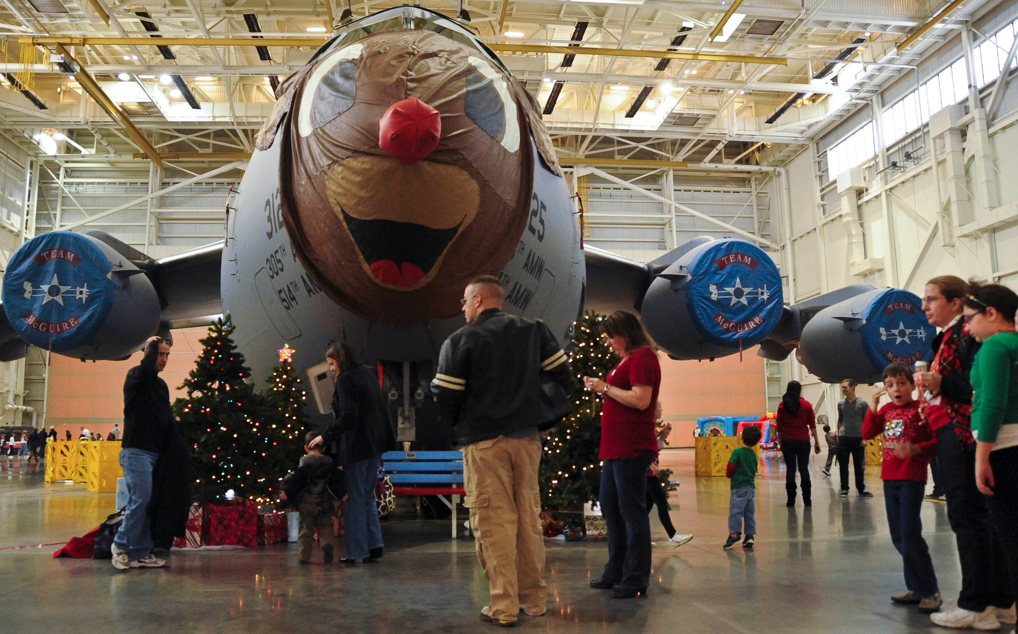 Servicemembers and their families wait to take photos underneath a C-17 Globemaster III; a bench was set up underneath the nose of the aircraft so families could take photos Dec. 3 at Dock 1 for a unit holiday party. The 305th Operations Group and 305th Maintenance Group provided facilities, support and manpower to host this event, while the spouse of the Airmen organized, planned and executed the event. Dock 1 was filled with a variety of activities for families and their children such as: face painting, fishing pond, cake walk, bouncy houses, craft table and football throw station. (U.S. Air Force photo by Airman 1st Class Dennis Sloan/Released)