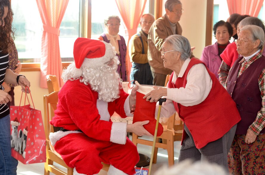 A member of the Wolf Pack dressed as Santa Claus, gives a stocking to a resident of the Heart of Jesus Senior Care elderly home during his visit there for a Christmas celebration in Gunsan City, Republic of Korea, Dec. 10, 2011. The senior center was host to many smiles, cake, joint decorating and singing classic Christmas carols. (U.S. Air Force photo by Senior Airman Derrick Schwieters/Released)