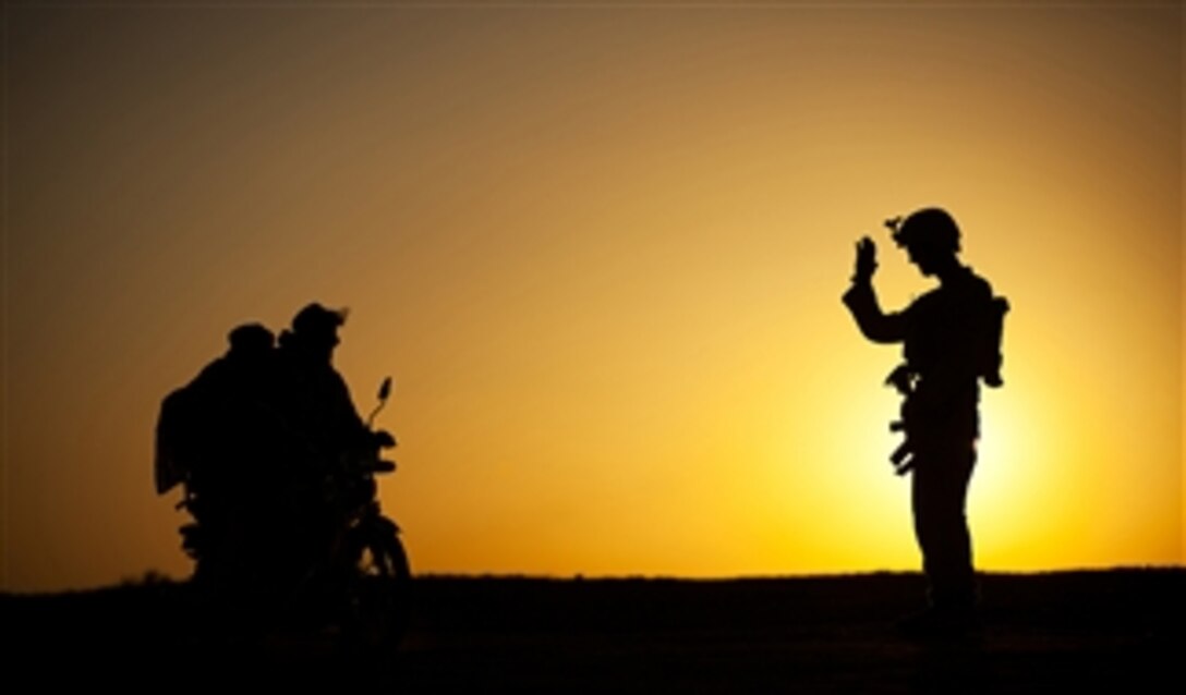 U.S. Marine Corps Lance Cpl. Phil Schiffman, a mortarman with Weapons Company, 3rd Battalion, 3rd Marine Regiment, waves to two Afghan men on a motorcycle after searching them at a vehicle checkpoint in Sar Bandadar, Garmsir district, Helmand province, Afghanistan, on Dec. 1, 2011. The vehicle checkpoints were a regular part of the mortarmen's duty rotation, which also includes security patrols and guard duty.  