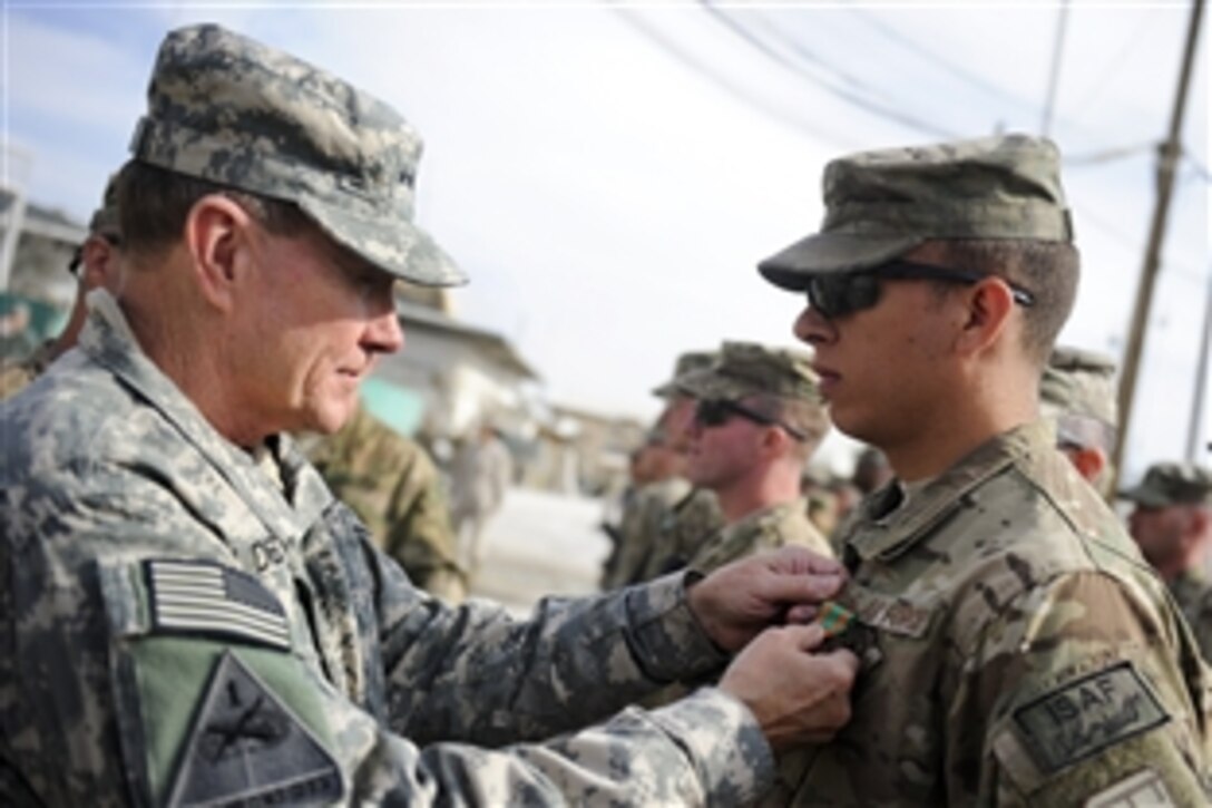 U.S. Army Gen. Martin E. Dempsey, chairman of the Joint Chiefs of Staff, left, presents a Navy Commendation Medal to an airman at Camp Nathan Smith, Afghanistan, Dec. 16,  2011.  