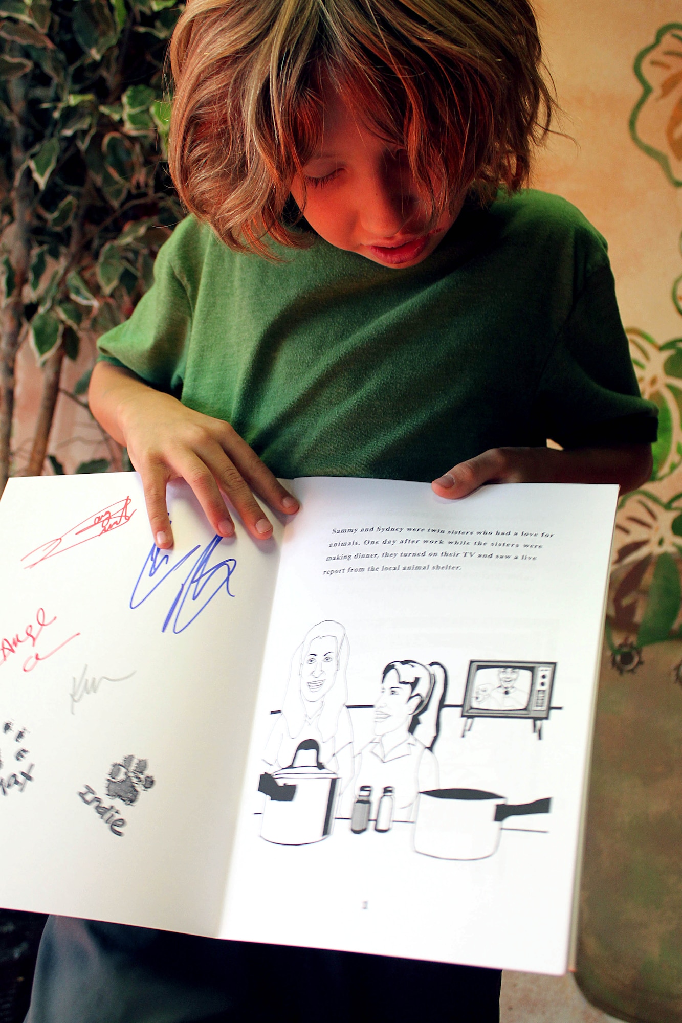 Keaton Withrow, 9, reads the first page of Max and Indie Come Home after showing his family the autographs of Kerry Moynahan, Doug Brochu and Chris Brochu on the inside cover Dec. 16. (U.S. Air Force Photo by Meredith Mingledorff) 