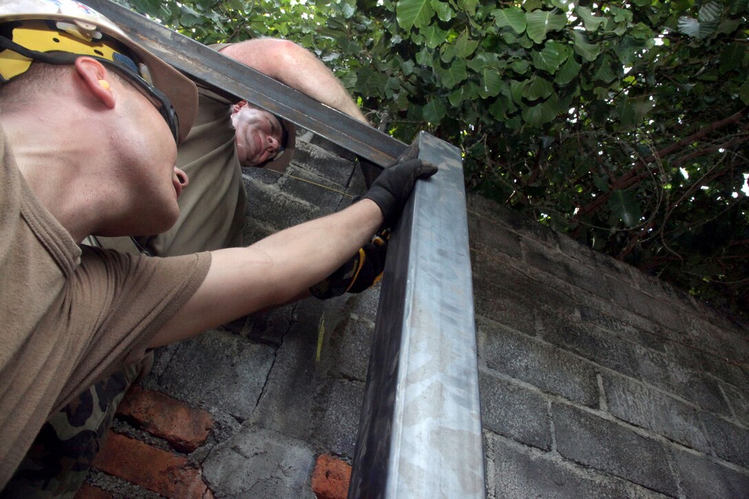 U.S. Navy Petty Officer 1st Class Bruce Nisbet and Petty Officer 2nd Class Michael McAfee  hold and drill two beams for a shed at Escuela de Educacion Parvularia Maria Luisa Marcia in La Union, El Salvador, Dec. 16, 2011. Nisbet, a utilities man, and McAfee, an equipment operator, are assigned to Navy Mobile Construction Battalion 23.