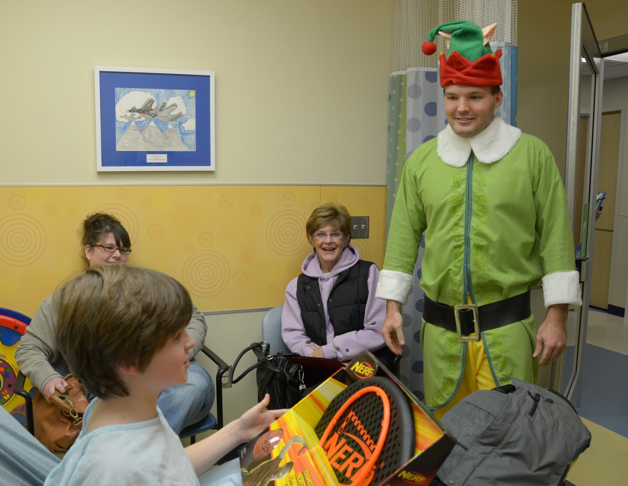 WRIGHT-PATTERSON AIR FORCE BASE, Ohio - Buddy the Elf, an “honorary” member of the 87th Aerial Port Squadron, delivers a Christmas present to 11-year-old Gabe Atkins, a patient at Dayton Children’s Hospital, Dec. 16. 87APS members have worked with the hospital for more than 22 years to bring a little more happiness to children who are hospitalized there over the holidays. (U.S. Air Force photo/Capt. John Stamm)