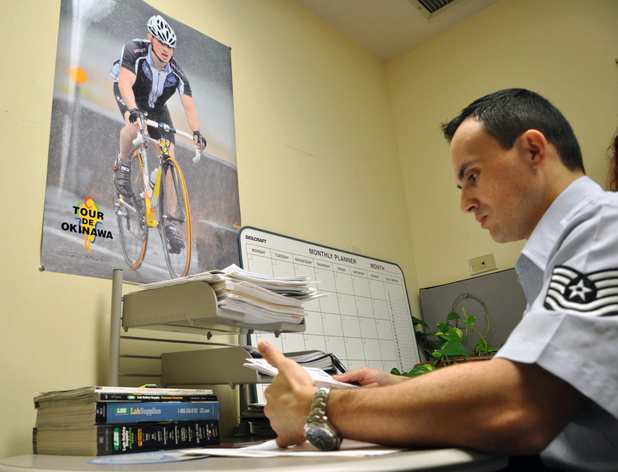 LAUGHLIN AIR FORCE BASE, Texas— Tech. Sgt. Edgar Ferreira, 47th Medical Support Squadron NCO in-charge of laboratory services, takes care of paperwork in his office here Dec. 19, where a poster of him cycling in Japan serves as a reminder of how far he has come. Ferreira was the victim of a drunk driver Dec. 7, 2007, an event that left him with a compound femur fracture and two broken knee caps which he has made a full recovery from. (U.S. Air Force photo/2nd Lt. James Ramirez)
