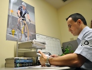 LAUGHLIN AIR FORCE BASE, Texas— Tech. Sgt. Edgar Ferreira, 47th Medical Support Squadron NCO in-charge of laboratory services, takes care of paperwork in his office here Dec. 19, where a poster of him cycling in Japan serves as a reminder of how far he has come. Ferreira was the victim of a drunk driver Dec. 7, 2007, an event that left him with a compound femur fracture and two broken knee caps which he has made a full recovery from. (U.S. Air Force photo/2nd Lt. James Ramirez)