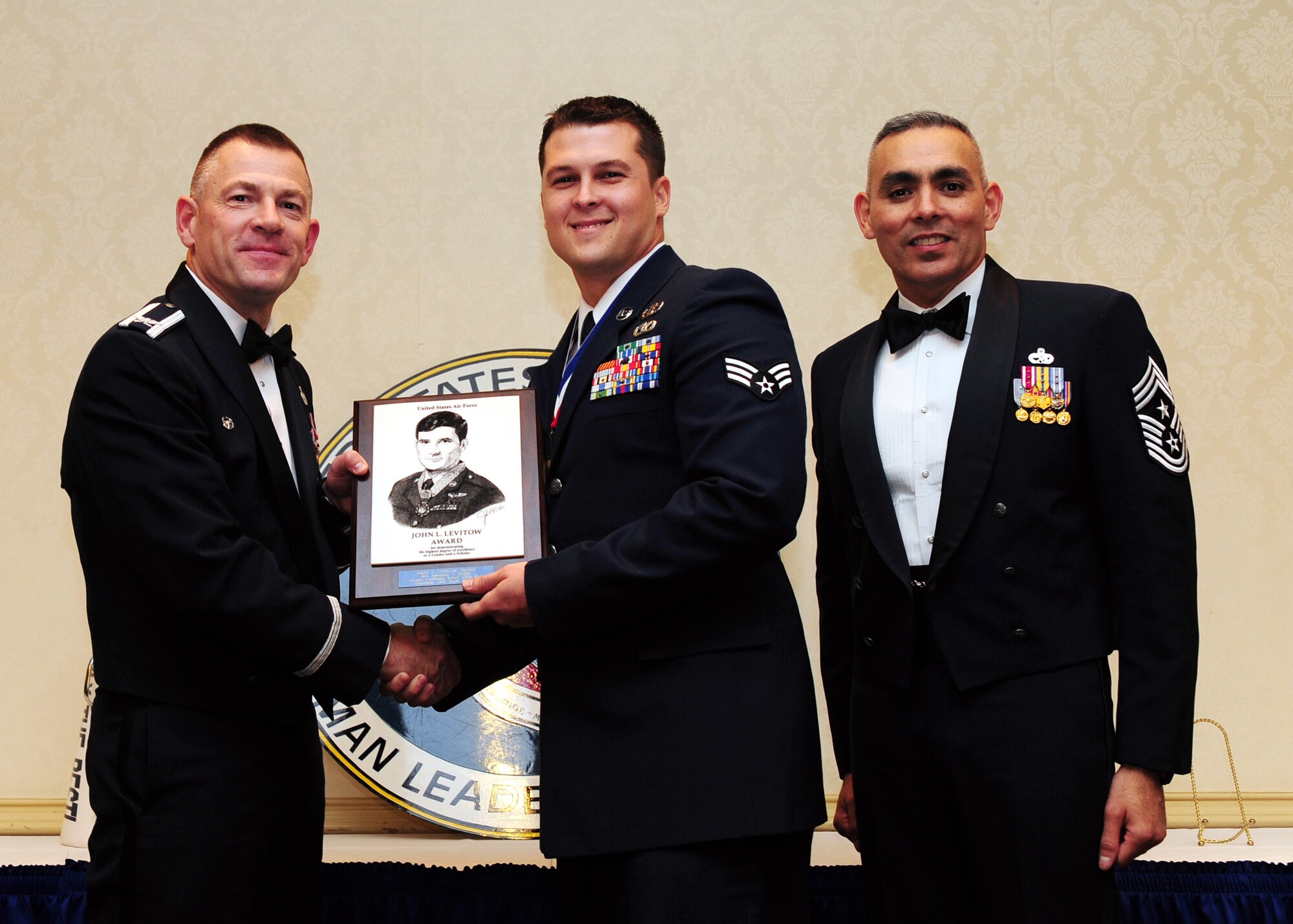 Col. Richard McComb and Chief Master Sgt. Jose LugoSantiago present the John L. Levitow Award to Senior Airman Johnathan Baxley during the Airman Leadership School Class graduation at Joint Base Charleston - Air Base Dec. 15. The award is presented to the student who displays exemplary excellence as both  a leader and a scholar. McComb is the JB Charleston commander and LugoSantiago is the 628th Air Base Wing command chief. Baxley is an explosive ordnance disposal journeyman assigned to the 628th Civil Engineer Squadron. (U.S. Air Force photo/Staff Sgt. Katie Gieratz) 
