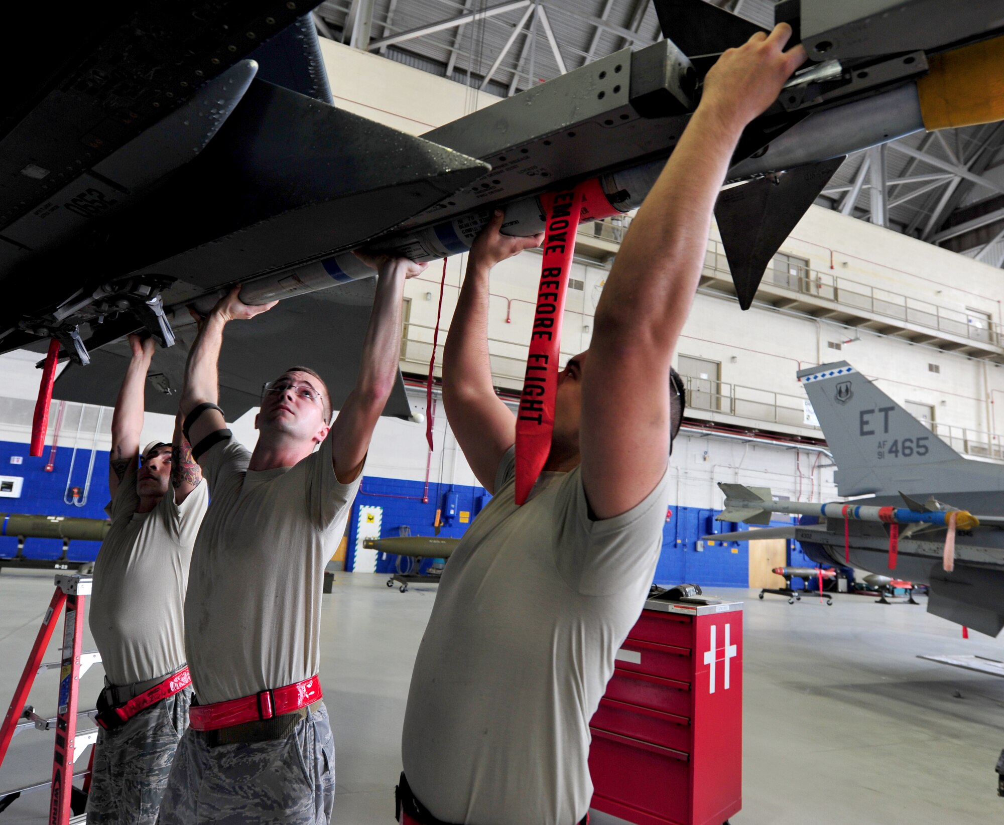 Senior Airman Hector Vazquez and Staff Sgt. Kenneth Merritt, from the 46th Aircraft Maintenance Squadron, hold the weapon as Airman 1st Class Christopher Rose performs final adjustments to the AIM-9 during the 46th Maintenance Group’s fourth quarter weapons load competition at Eglin Air Force Base, Fla., Dec. 21. The best of Blue AMU and Red AMU met to load an AIM-9 and GBU-12 onto an F-16 and F-15 respectively. AMU Red won the competition. (U.S. Air Force photo/Randy Gon) 