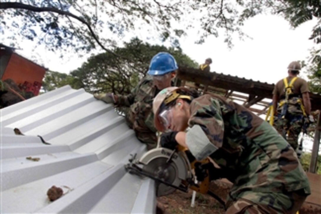 U.S. Navy Petty Officer 2nd Class Rejuny Caswell (right) cuts aluminum panels with Salvadoran marine Patriz Gutierrez for the roof of an open classroom and pavilion at Centro Escolar Elementary School in La Union, El Salvador, on Dec. 13, 2011.  Caswell is a steel worker assigned to Navy Mobile Construction Battalion 23.  