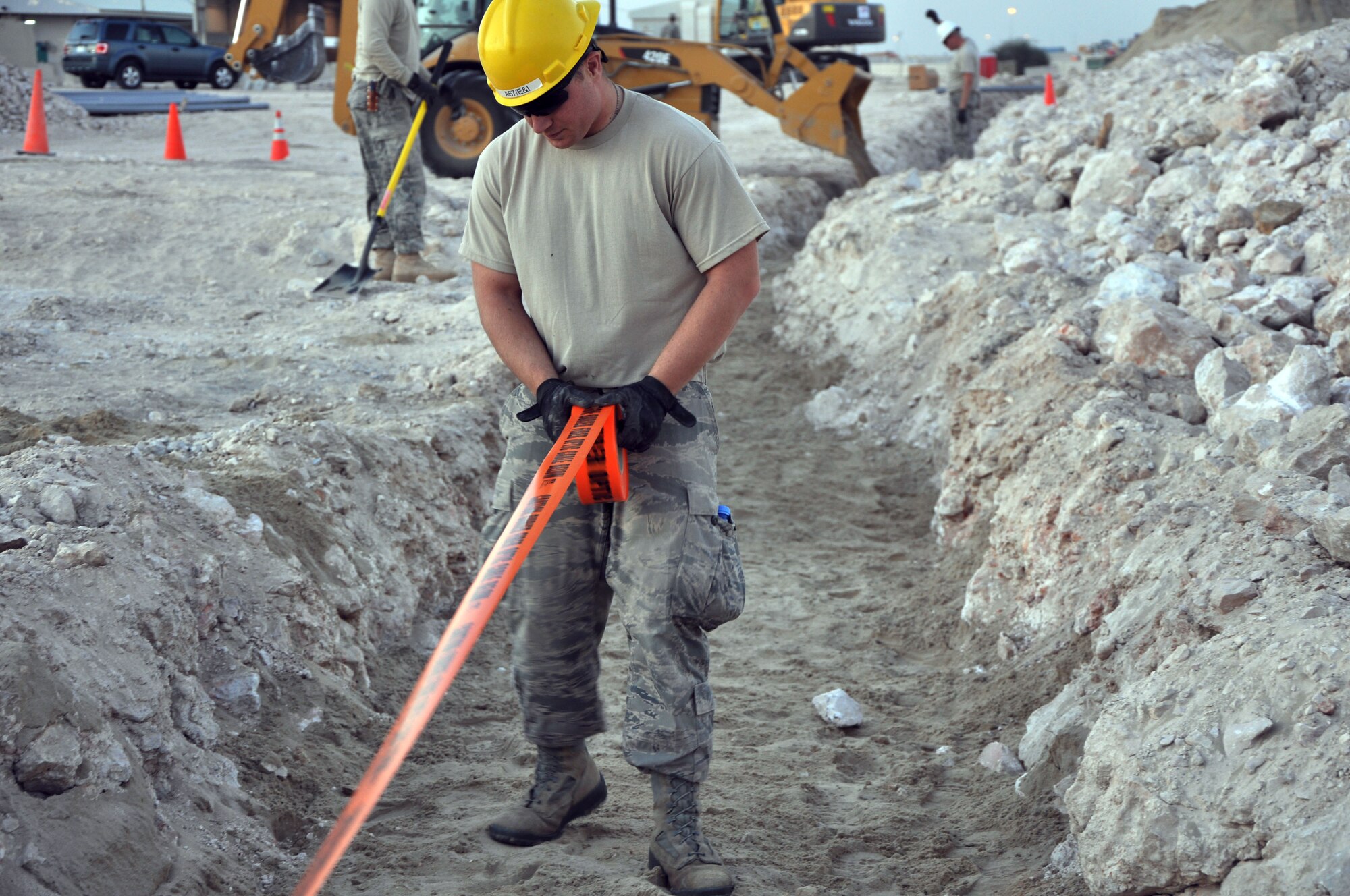 Airman 1st Class Christian Blaydon, A67 Engineer and Installation team member deployed from the Pennsylvania Air National Guard, lays down warning tape over sand that covers a newly replaced ground tactical fiber run Dec. 19, 2011. The team worked for four days to replace the communications line, which provides connectivity from one section of the base to another, with a permanent and more secure underground conduit. Blaydon is a native of Horsham Township, Pa. (U.S. Air Force photo/Senior Airman Michael Charles)