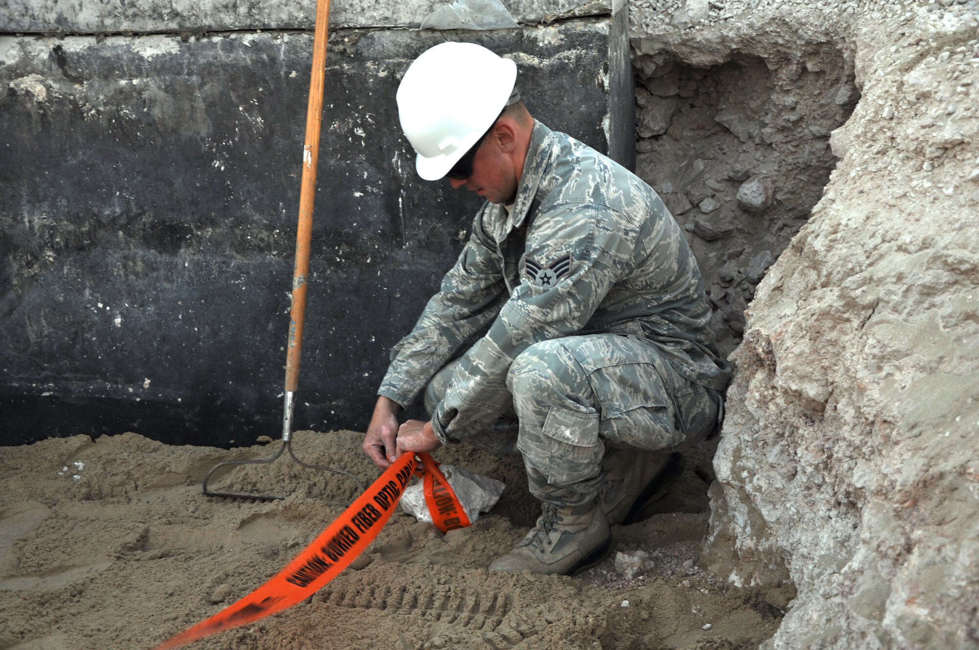 Senior Airman Mark Wojdylo, A67 Engineer and Installation team member deployed from the Pennsylvania Air National Guard, secures warning tape over sand that covers a newly replaced ground tactical fiber run Dec. 19, 2011. The team worked for four days to replace the communications line that provides connectivity from one section of the base to another with a permanent and more secure underground conduit. Wojdylo is a native of Lyndon, Pa. (U.S. Air Force photo/Senior Airman Michael Charles)