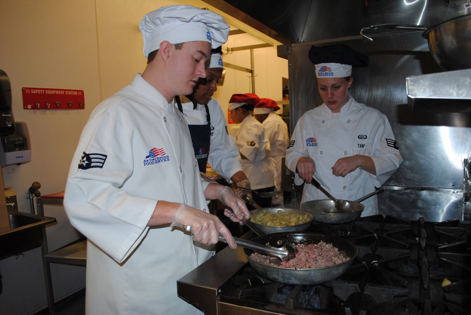 Senior Airman Brenton Schmidt, missile chef with the 490th Missile Squadron, cooks sausage for his sausage apple stuffing, while Senior Airmen Chariesse Garret and Kara Tank, missile chefs with the 10th Missile Squadron, prepare pork chops stuffed with gorgonzola cheese and apples.