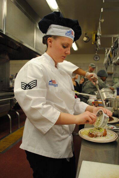 Senior Airman Kara Tank, missile chef with the 10th Missile Squadron, gently dribbles cheese on top of pork chops for her dish. (U.S. Air Force photo/Airman 1st Class Katrina Heikkinen)

