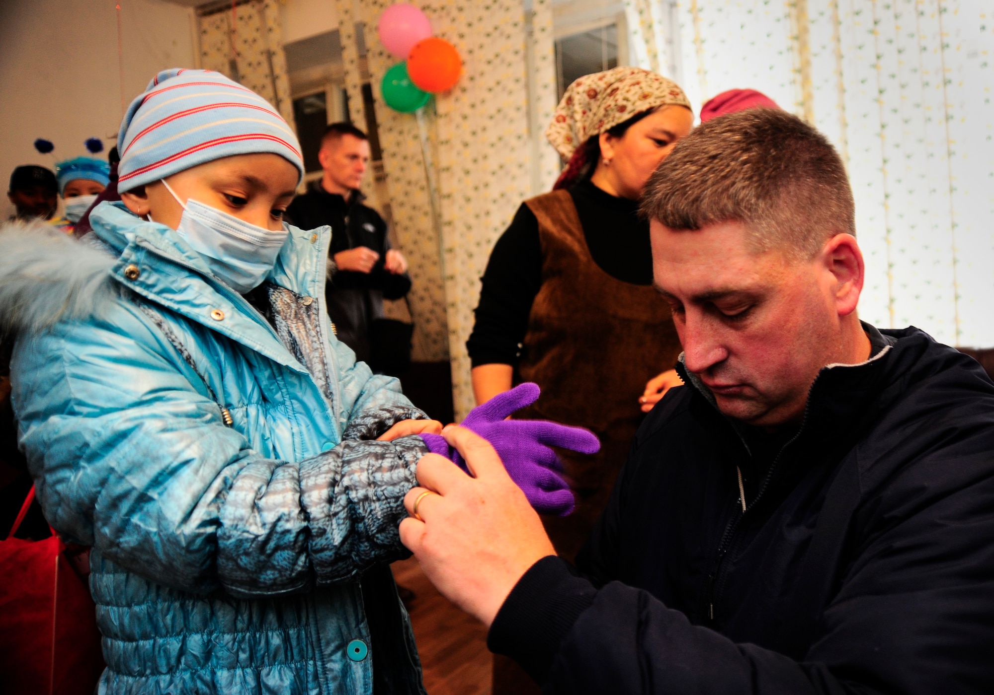 Tech. Sgt. James Berger fits gloves and a winter coat on a girl Dec. 28, 2011, at the Children's Cancer Center in Bishkek, Kyrgyzstan during "Operation Warm and Dry." The Manas Area Benefit Outreach Society distributed more than 40 winter coats and blankets to the center on behalf of the Transit Center at Manas, the Kyrgyz Republic and the U.S. Embassy as part of a partnership called "Operation Warm and Dry."  Berger is with the 376th Expeditionary Civil Engineer Squadron and is deployed here from 182nd Airlift Wing Peoria, Ill.(U.S. Air Force Photo/Staff Sgt. Angela Ruiz)